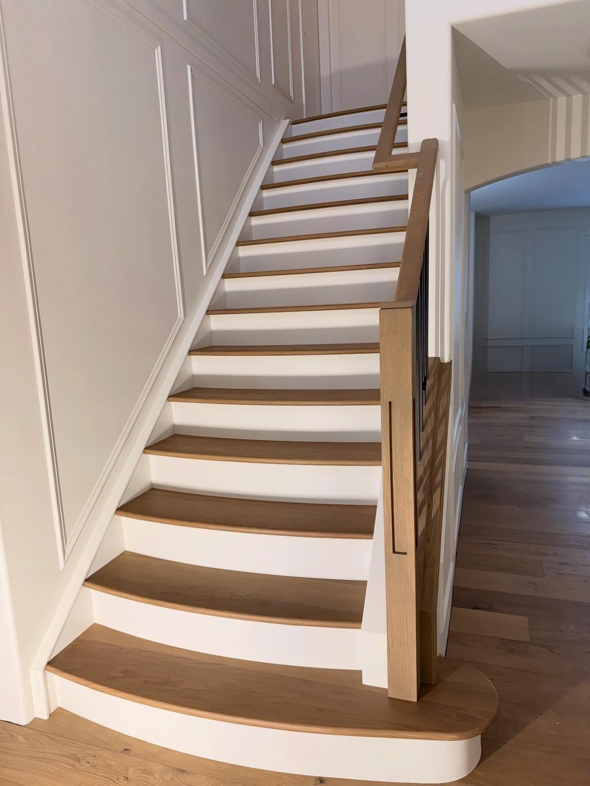 Custom curved hardwood stairs with white risers, viewed from the side.