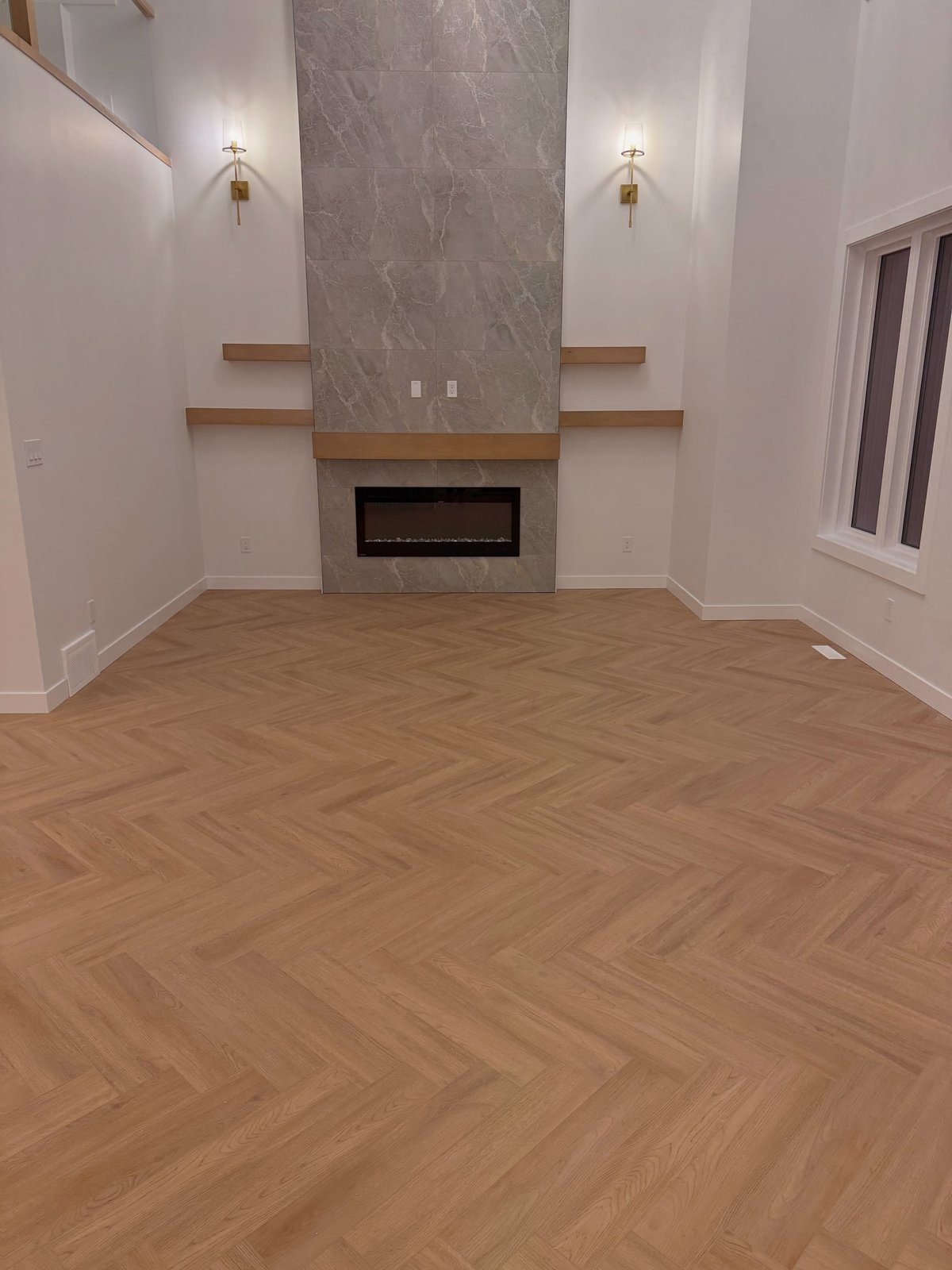 Light brown herringbone-pattern flooring across a room, extending toward a tall fireplace surround.