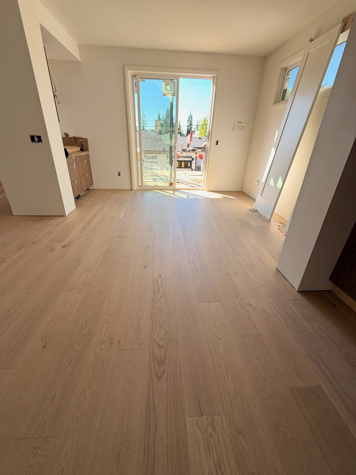 Light beige plank flooring with staggered joints leading toward a glass exterior door.