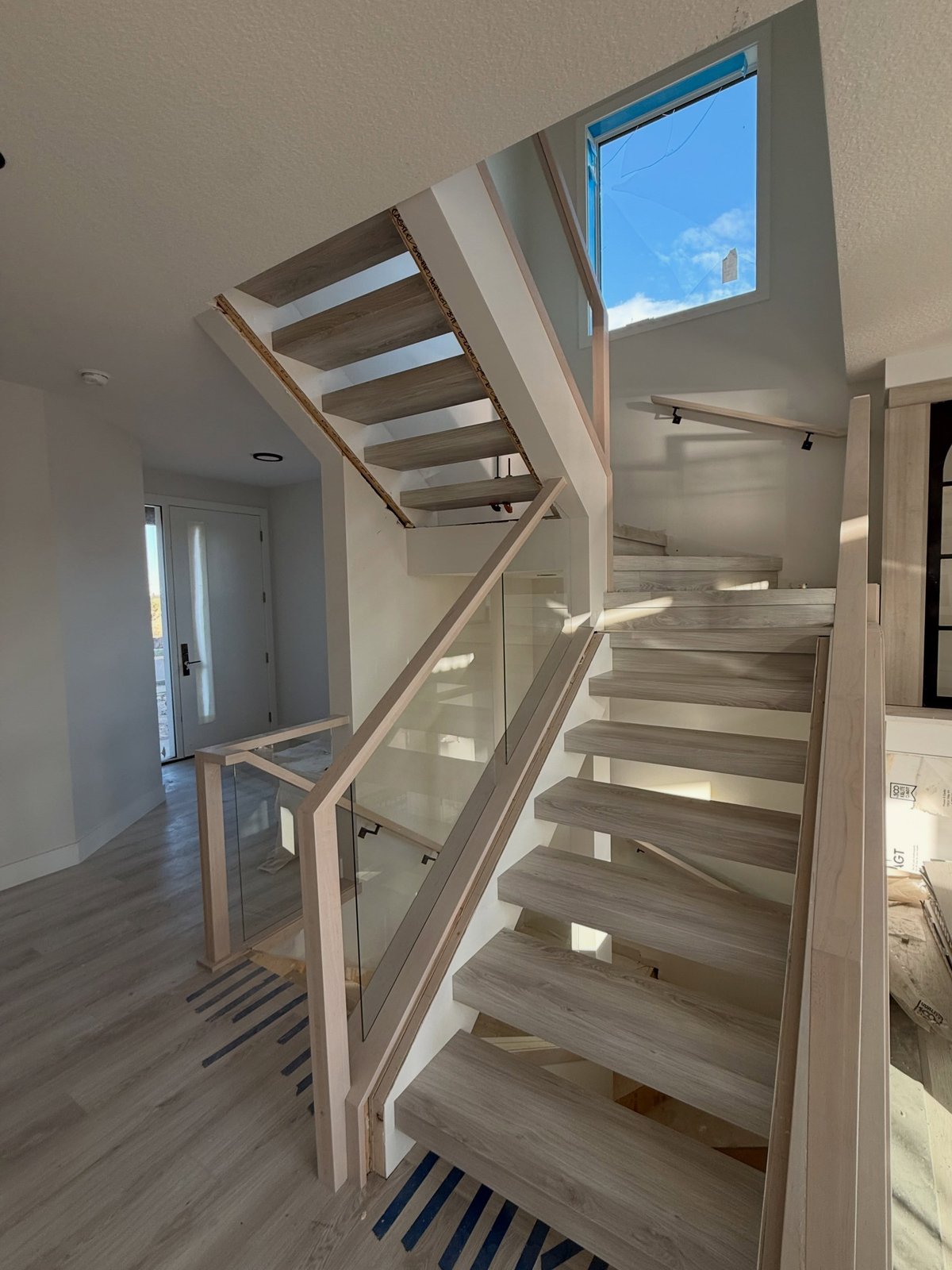 Pale wood-toned open-riser stairs with wedge-shaped turning steps and another stair flight overhead.