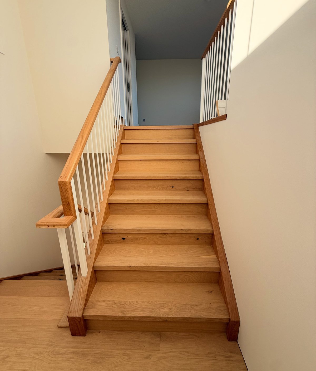 Straight staircase with golden-brown wood-toned treads and risers above a similarly toned floor.