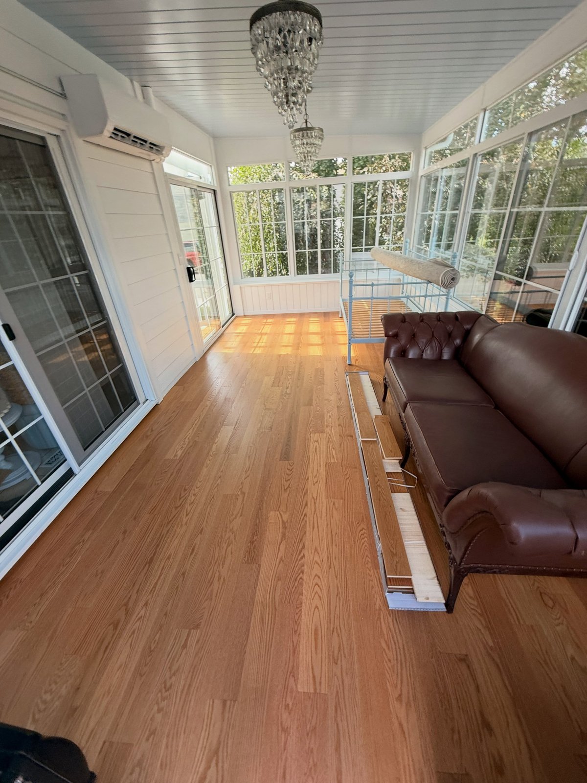 Warm brown plank flooring in a window-lined room, with a sofa and loose boards along the right side.